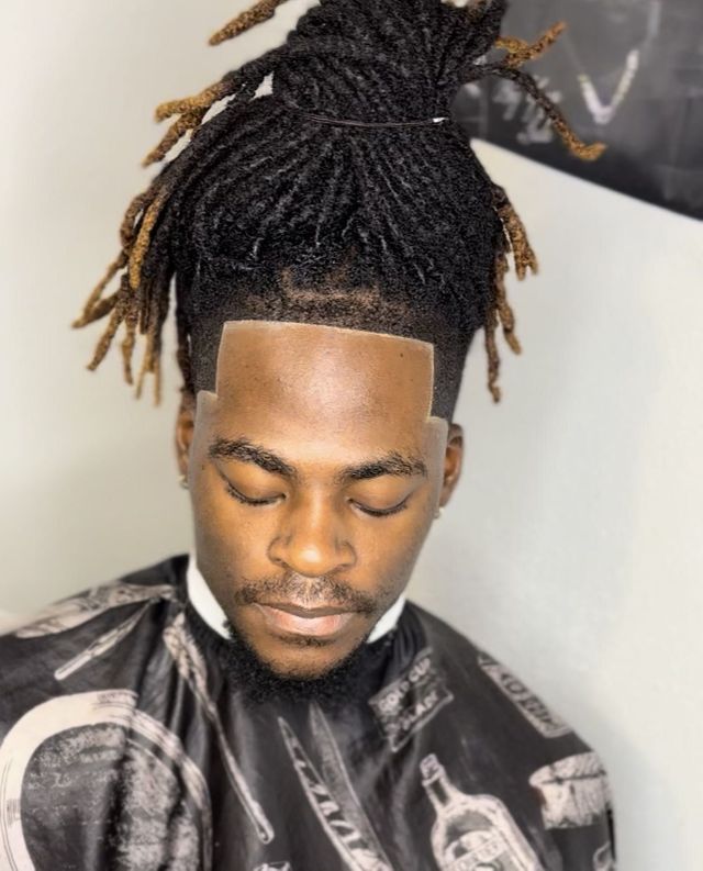 Client with long dreadlocks tied in a top bun, sharp forehead lineup and temple fade, small beard